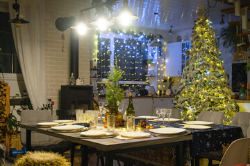 Festive interior of house is decorated for Christmas and New Year in loft style with black stove, fireplace, Christmas tree. Warm studio room with set table, burning wood, cozy and heating of home