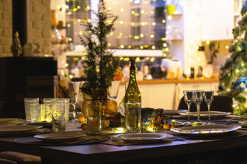 A festive table set for guests for Christmas and New Year, a Christmas tree in the living room, plates, bottles, glasses, potted plants, fairy lights