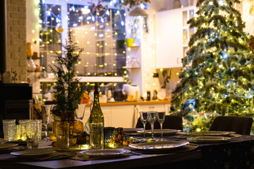 A festive table set for guests for Christmas and New Year, a Christmas tree in the living room, plates, bottles, glasses, potted plants, fairy lights