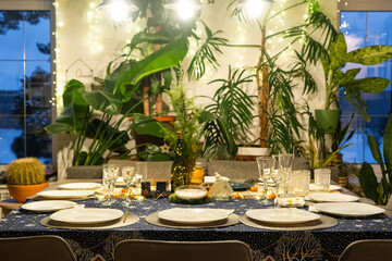 A festive table set for guests for Christmas and New Year, in the living room, plates, bottles, glasses, potted plants, fairy lights