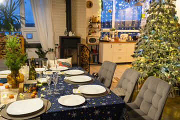 Festive interior of house is decorated for Christmas and New Year in loft style with black stove, fireplace, Christmas tree. Warm studio room with set table, burning wood, cozy and heating of home