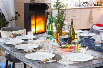 Festive interior of house is decorated for Christmas and New Year in loft style with black stove, fireplace, Christmas tree. Warm studio room with set table, burning wood, cozy and heating of home