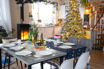 Festive interior of house is decorated for Christmas and New Year in loft style with black stove, fireplace, Christmas tree. Warm studio room with set table, burning wood, cozy and heating of home