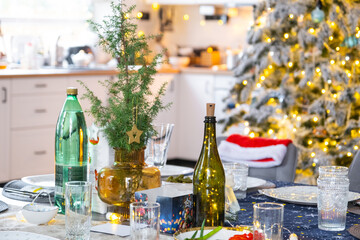 A festive table set for guests for Christmas and New Year, a Christmas tree in the living room, plates, bottles, glasses, potted plants, fairy lights
