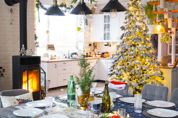 Festive interior of house is decorated for Christmas and New Year in loft style with black stove, fireplace, Christmas tree. Warm studio room with set table, burning wood, cozy and heating of home