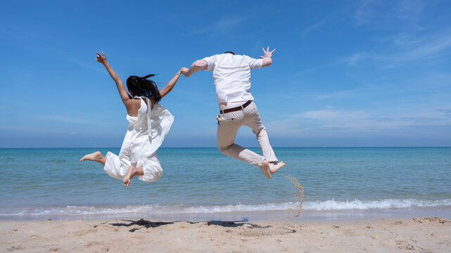 Happy couple jumping together on a tropical beach under a bright blue sky, symbolizing freedom, joy, and love. Perfect for travel, vacation, honeymoon, lifestyle, and summer inspiration concepts.