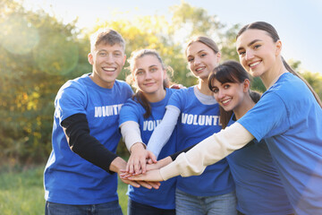 Group of happy volunteers stacking hands in park