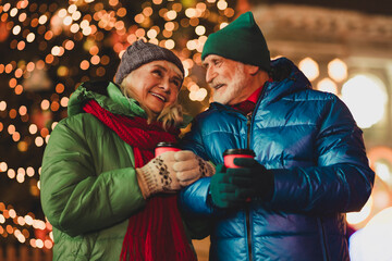 Joyful elderly couple enjoying a warm holiday night outdoors in winter city scene with Christmas...