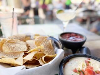 Freshly made tortilla chips with queso dip and salsa served in a lively outdoor restaurant setting during a sunny afternoon