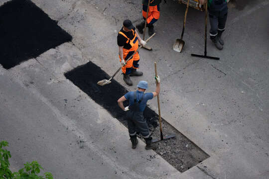 Road construction workers repairing damaged asphalt pavement with shovels and rakes, focused on restoring urban infrastructure and safety