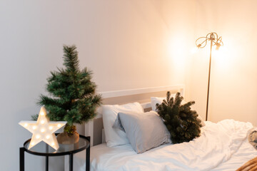 bedroom christmas decor. home interior for new years celebration. festive wreath, christmas tree. white sheets. pretty