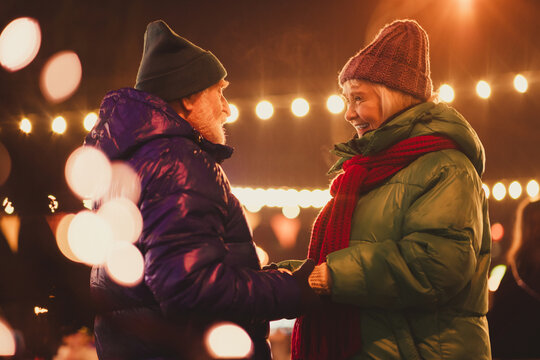 Funny winter moment as a couple of seniors share a warm smile under festive lights at a Christmas outdoor market - Powered by Adobe