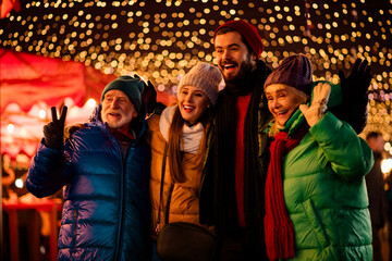 Joyful group of friends and family at a festive outdoor market glowing with lights during winter holiday season smiles and celebrates Christmas together