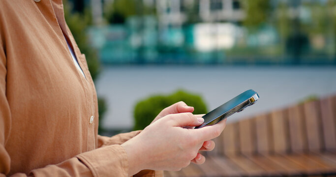 Side view of close up females hands using smartphone, typing a message or dialing number on the screen. Outdoors.