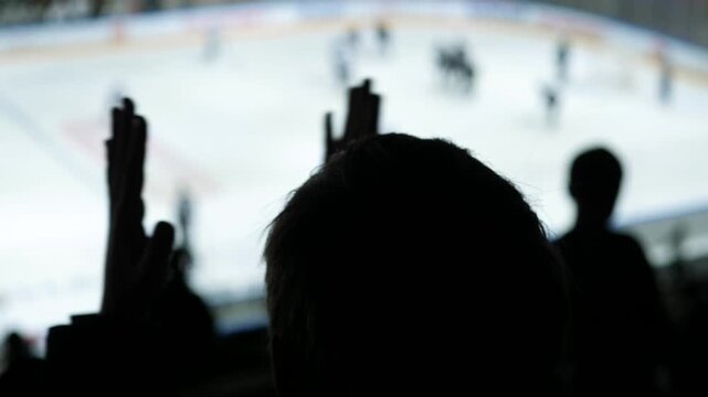 Silhouette of young boy hockey fan clapping on stands at ice match, child watching game in arena atmosphere