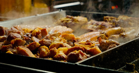 Delicious fatty pork meat and sausages cooking on large hot oily pan, releasing greasy smoke