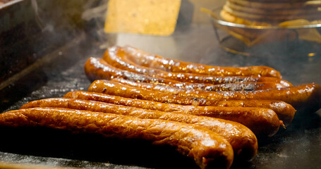 Sizzling sausages grilling on hot plate, releasing smoky aroma and appetizing golden brown crust while cooking over intense heat
