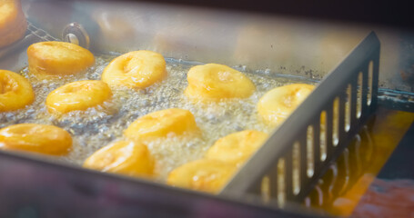 Automated donut production line featuring golden pastries deep frying in bubbling hot oil at industrial bakery manufacturing facility