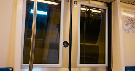Moving through a subway, reflections appear in the glass of a door, highlighting the dynamic atmosphere of public transport at night while commuters enjoy their travel.