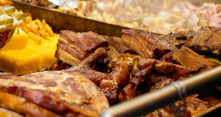 Close up of various grilled meat street food, including pork belly, sausages, and polenta, cooking on a hot plate