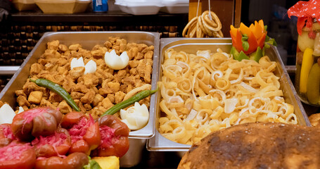 Metal trays containing crispy pork skin and chicharron, garnished with chili peppers and onions, displayed at a street food stall