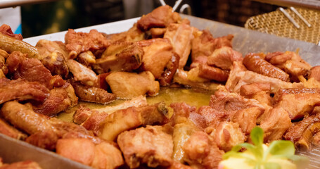 Close up of various fried street foods, including spare ribs and sausages, being served from a metal tray