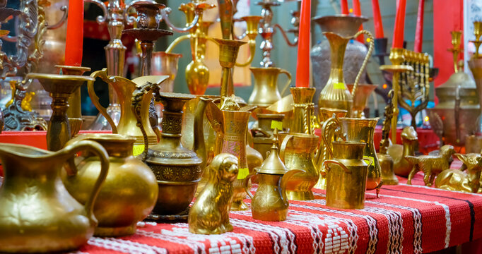 Antique brass items, including jugs, teapots, and animal figurines, are displayed on a table with a red and white tablecloth