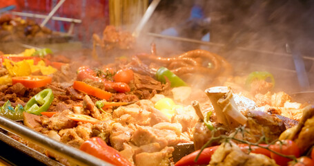 Street food vendor preparing sizzling meat and vegetables on hot cast iron griddle, releasing aromatic steam from traditional culinary display