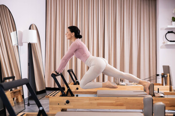 In an elegant studio, a woman engages her core while practicing Pilates on a reformer, demonstrating focus and determination with a serene, stylish backdrop.