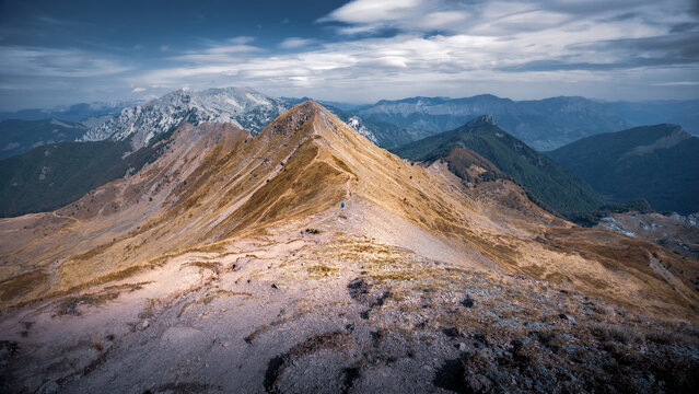 Female hiker walks narrow path to sunlit hilltop mountain ridge sunny day, Prokletije, Montenegro