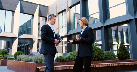 Smiling mature male and female colleagues discuss work over business lunch and shaking hands. Man businessman woman businesswoman in city handshaking shake hands partnership cooperation deal