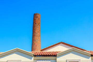 Fototapeta premium Historic brick chimney against clear blue sky of industrial building
