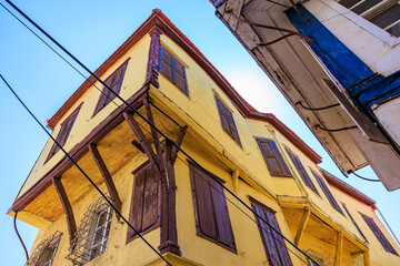 Historic yellow building with wooden shutters and overhangs against blue sky