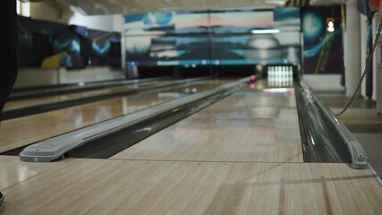 Female bowler approach and throws ball onto bowling lane, medium shot. Pink ball quickly moves down wooden, slippery lane, away from woman and toward pins.