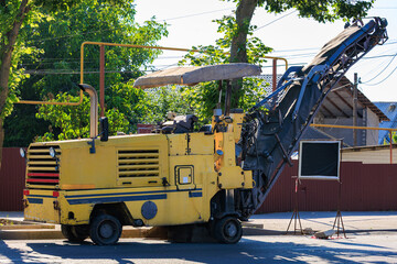 Yellow asphalt milling machine on urban street with trees and buildings
