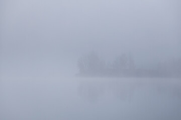 Foggy lake in the autumn morning. Quiet foggy morning. Fog over the autumn lake at the sunrise moment.