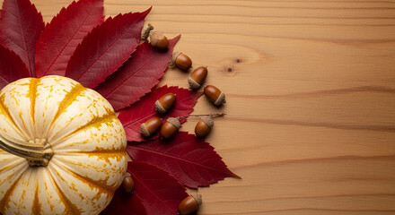 Overhead shot of a white pumpkin, red leaves, and acorns on wood, representing autumn harvest and Thanksgiving, perfect for holiday concept