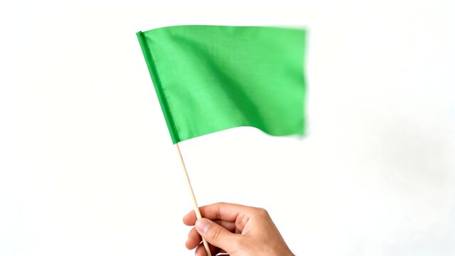Hand holding a small waving green flag on a stick. Isolated on white background