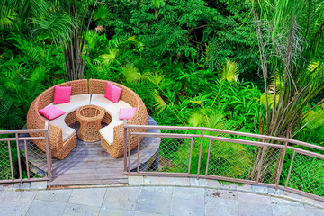 Obraz premium A circular rattan seating area with pink cushions against a backdrop of lush tropical plants in Yanoda Park, Sanya, Hainan, China