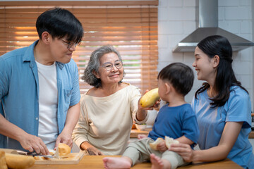 Happy Asian family preparing breakfast together in a cozy kitchen. Parents and toddler bonding while slicing bread and sharing food, reflecting love, care, and modern home lifestyle.
