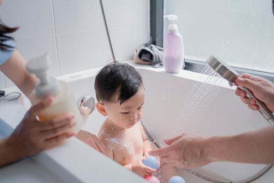 Asian parents lovingly bathing their adorable toddler in a bright bathroom, showcasing family bonding, daily routine, and tender parenting moments in a modern lifestyle setting.
