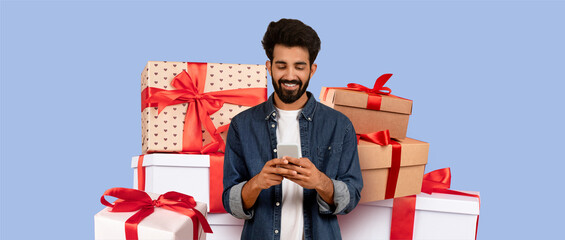 A man smiles while looking at his phone, surrounded by an array of colorful, gift-wrapped boxes with ribbons. It appears to be a festive occasion, filled with excitement and joy.
