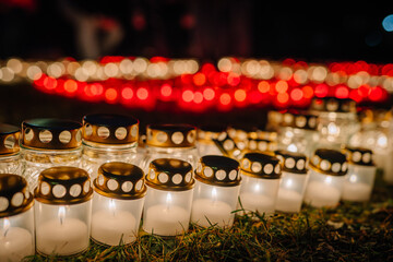 Glowing candles with golden lids are arranged in a beautiful pattern on the grass, creating a warm and inviting atmosphere during a nighttime celebration of remembrance