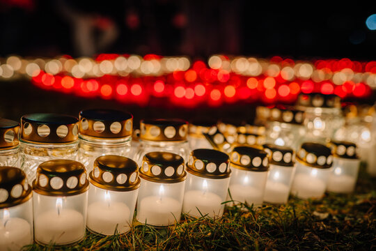 Glowing candles with golden lids are arranged in a beautiful pattern on the grass, creating a warm and inviting atmosphere during a nighttime celebration of remembrance