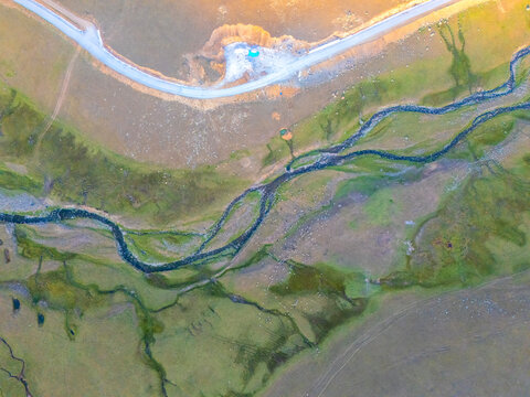Striking aerial abstract view of a high-altitude wetland or moorland, featuring a winding river and its tributaries cutting through green and beige, eroded terrain.