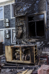 Ground level view of fire aftermath charred brick wall and damaged generator foreground twisted metal, shattered glass, and scorched AC units revealing intense destruction and electrical vulnerability