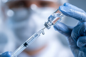 Scientist wearing protective gloves and a face mask preparing a vaccine by drawing liquid from a vial into a syringe in a clinical laboratory setting
