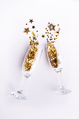 Festive Christmas and New Year composition with two champagne glasses with golden shining decorations and stars on white background top view. Christmas and New Year party concept.