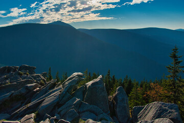 Karkonosze - widok ze Skalnego Stołu w kierunku masywu Śnieżki. Majestatyczny grzbiet górski ze skalistymi urwiskami i lasem sosnowym pod czystym, błękitnym niebem. © Pol Badger