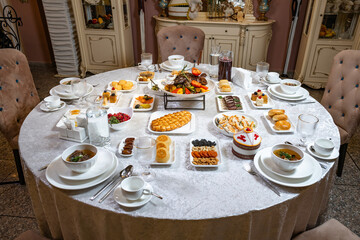 Luxury round banquet table with gourmet dishes, pastries and elegant silverware in classic interior